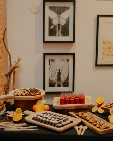 Mesa de fríos gourmet | Catering en Valencia Mesa decorada con postres y bebidas, rodeada de marcos con fotos en la pared.