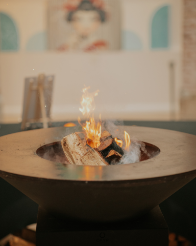 Ofyr con fuego encendido | Catering en Valencia Llama crepitante en un fogón moderno con fondo desenfocado.