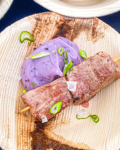 Brocheta de presa ibérica acompaña de cremoso parmentier de patata morada, presentada de forma gourmet para un evento elegante.