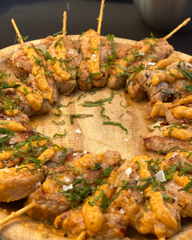 Brochetas de solomillo Duroc cocinadas al estilo gourmet, con leche de coco, curry rojo y menta, presentadas elegantemente para un evento.