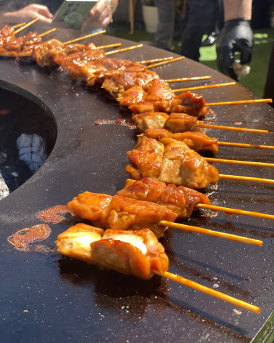 Brochetas de pollo marinado en Ofyr | Catering en Valencia Brochetas de pollo marinado asándose al fuego en Ofyr, presentadas de forma gourmet para un evento al aire libre.