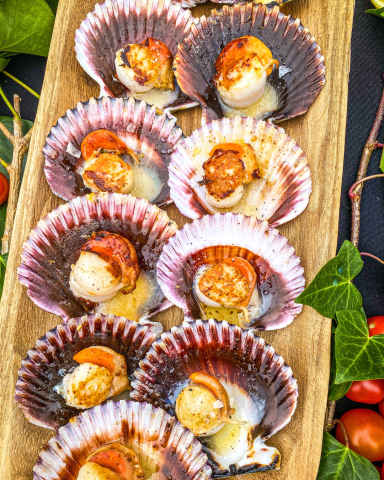 Zamburiñas cocinadas en la Ofyr con mantequilla clarificada y pimienta Sichuan, servidas de forma elegante para un catering gourmet.