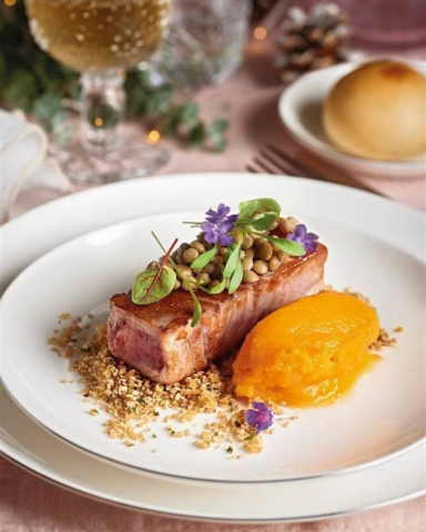 Plato gourmet con carne, puré de zanahoria y decoración de flores comestibles.